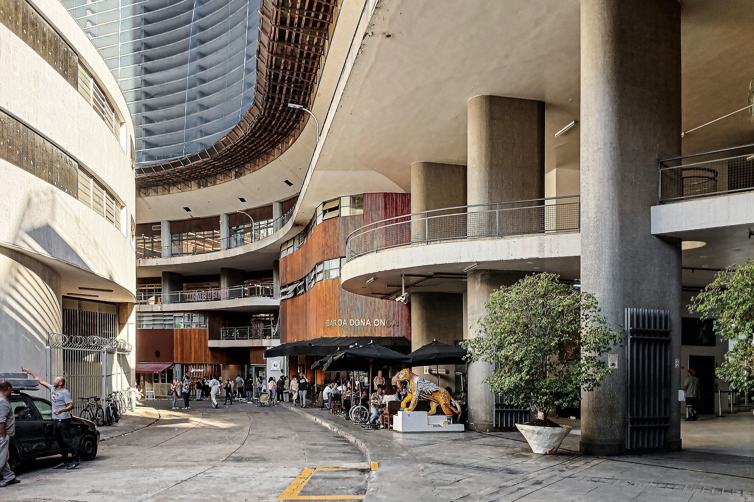 Un centro comercial de varios niveles con techo curvo, pilares grandes y zonas de estar al aire libre.