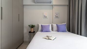 A modern bedroom with a large bed, a bedside table with a plant, and a wall-mounted air conditioner.