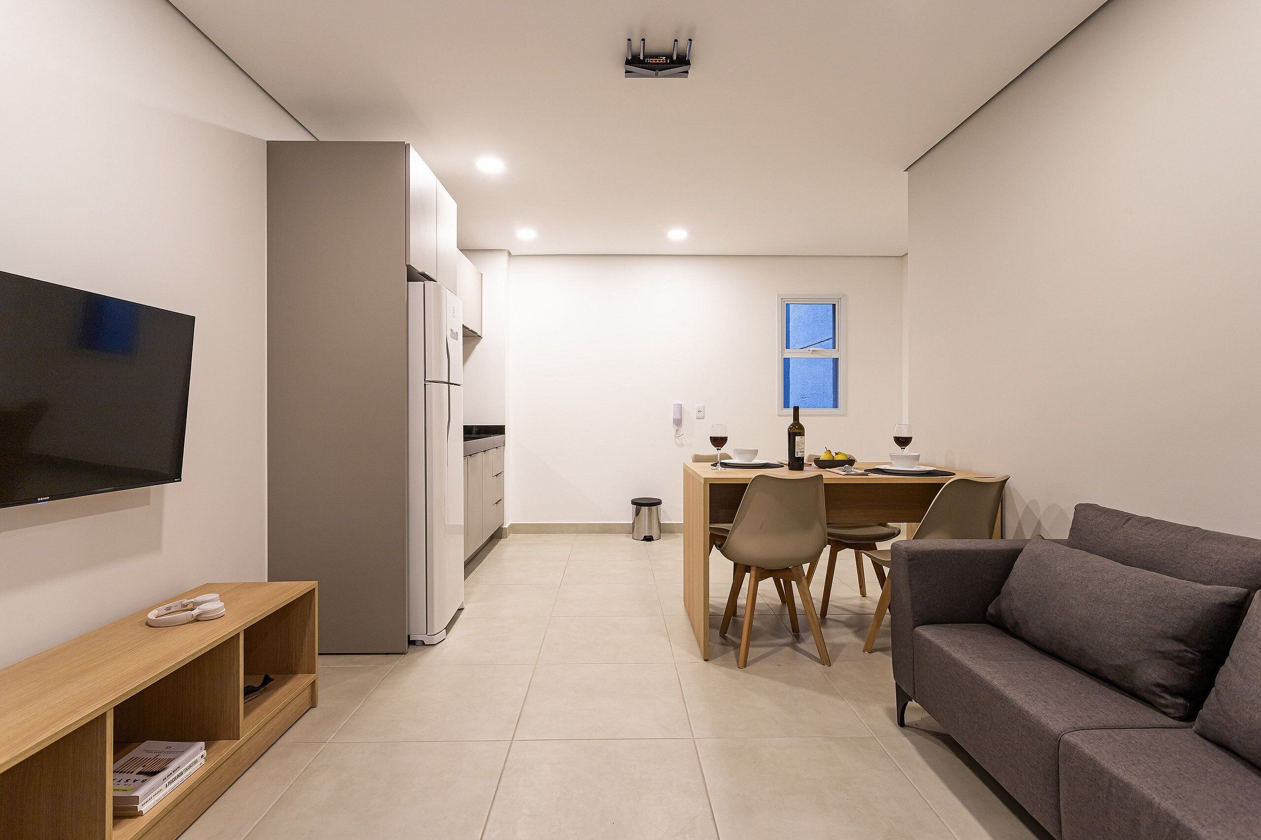 A modern living room with a flat-screen TV, a sofa, a wooden coffee table, and a dining area with a table and chairs.