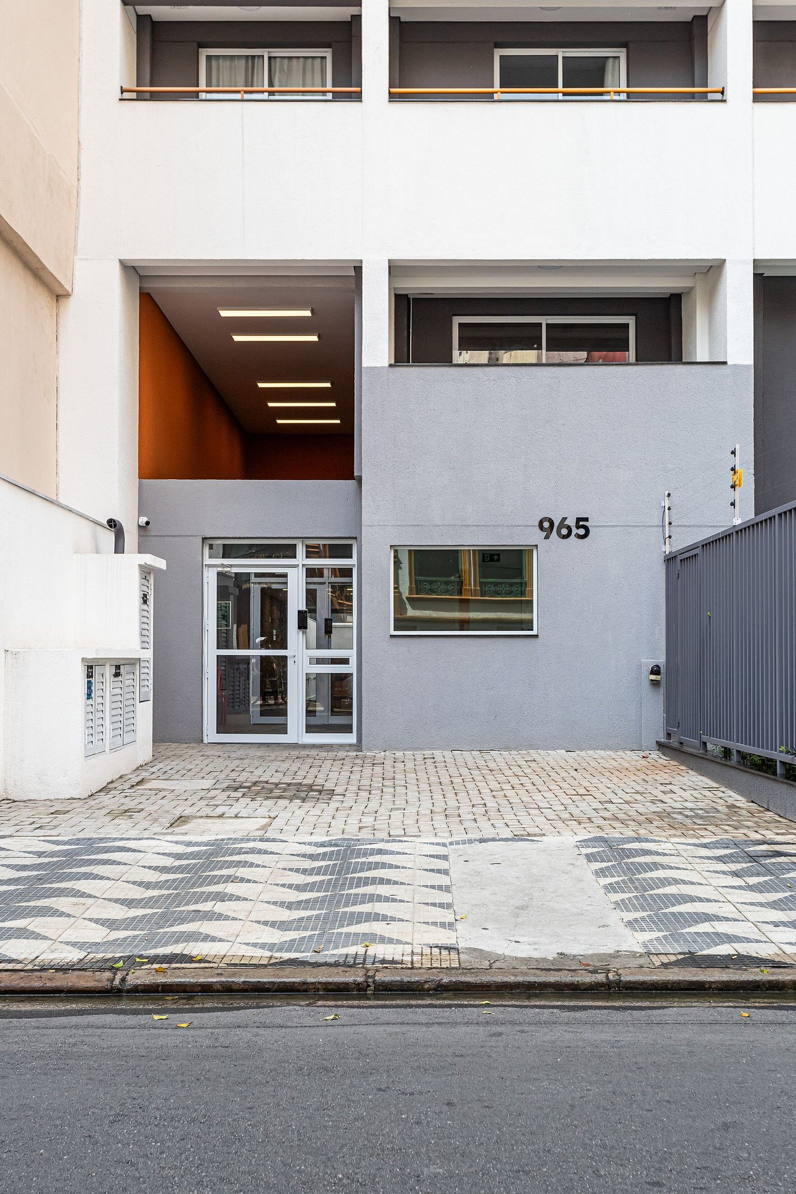 A modern building with a ground-level entrance, a visible number '965', and a tiled pavement.
