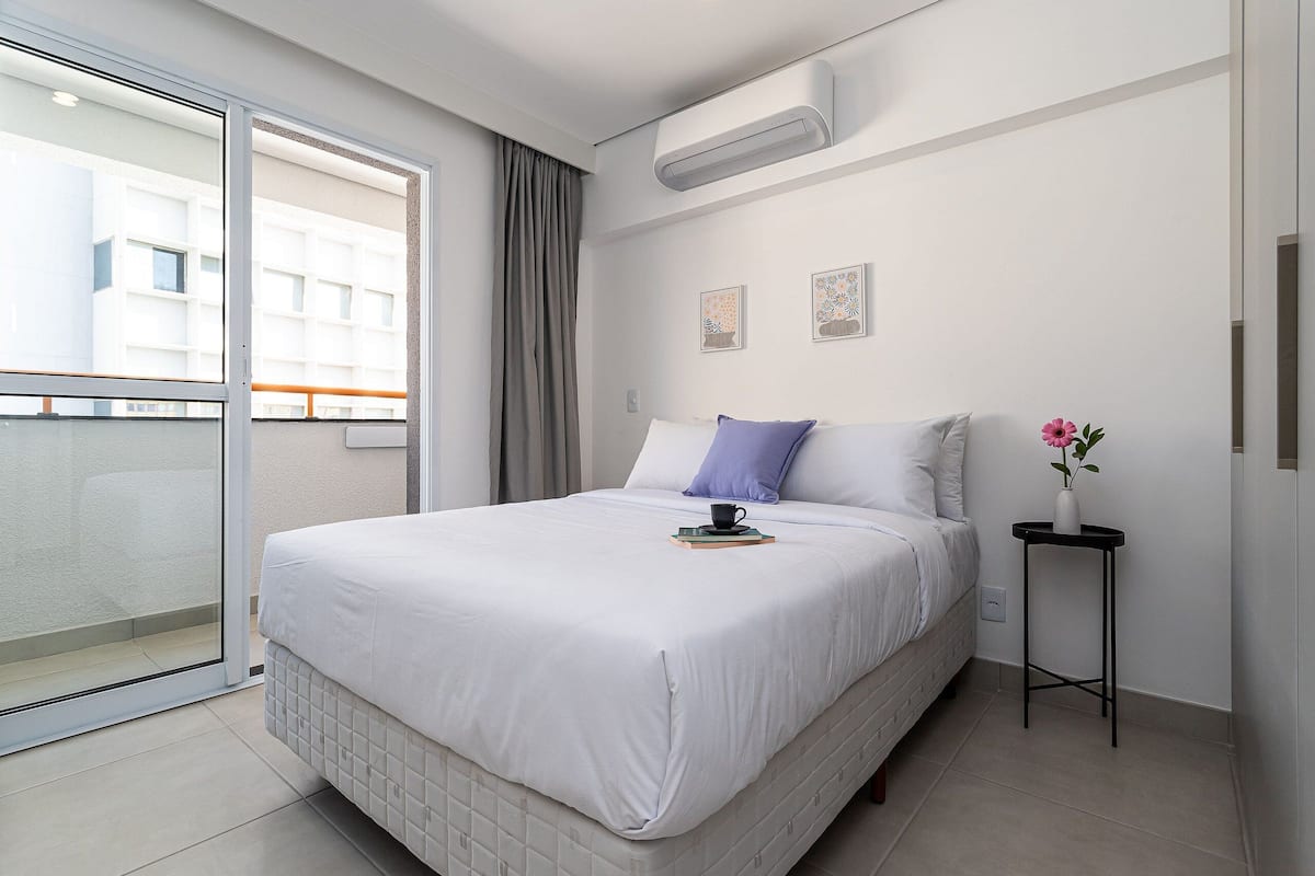 Et moderne hotelværelse med en stor seng, et lille sengebord og et vindue med udsigt til bygninger.