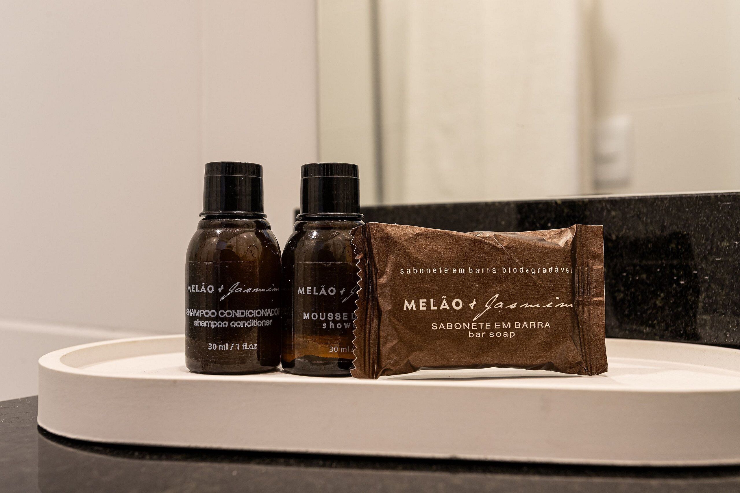 Tres botellas de champú, acondicionador y jabón MELÃO & Jasmin sobre una encimera de baño.