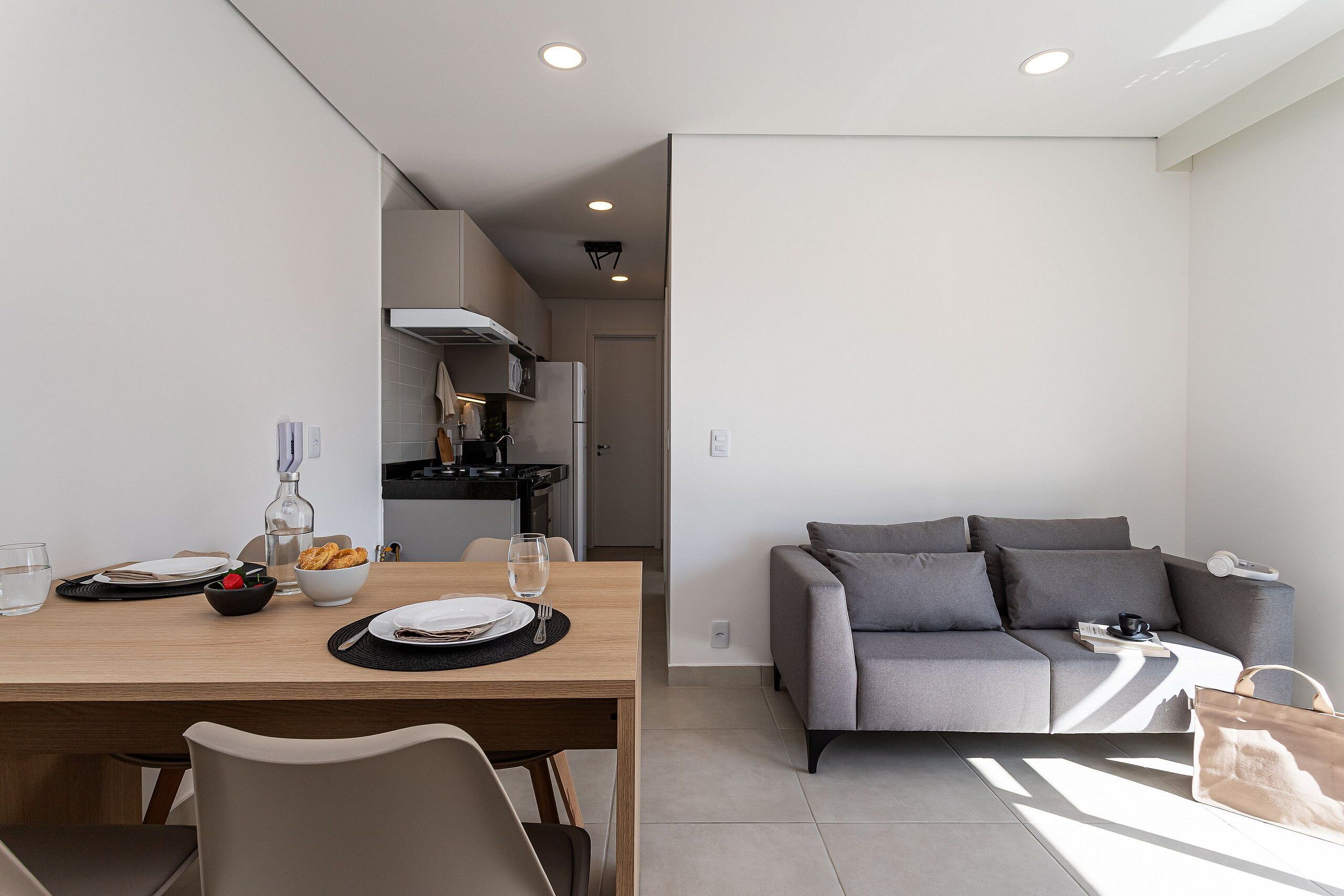 Una sala de estar moderna con un sofá gris, una mesa de comedor de madera dispuesta con platos, vasos y un tazón de fruta.