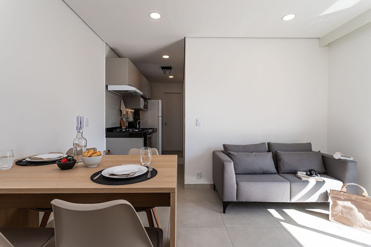 Una sala de estar moderna con un sofá gris, una mesa de comedor de madera dispuesta con platos, vasos y un tazón de fruta.