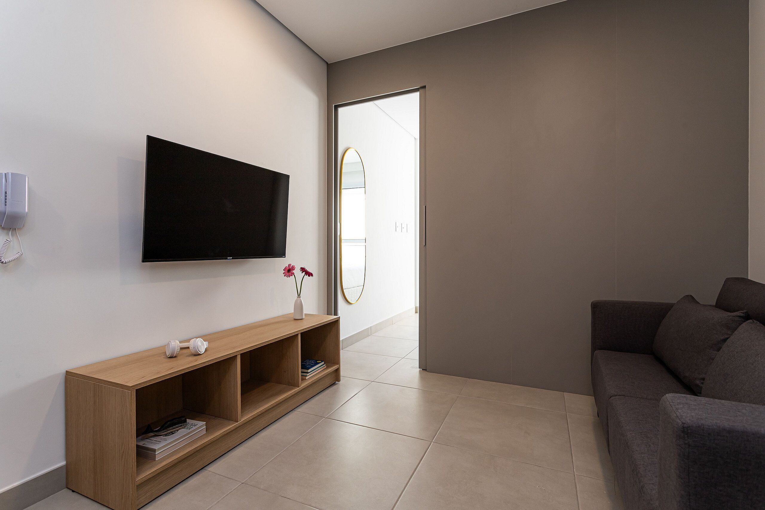 Ein modernes Wohnzimmer mit einem an der Wand montierten Flachbildfernseher, einem Holzkonsolentisch mit Dekorationen und einem grauen Sofa.