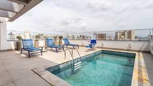 Zona de piscina en la azotea con sillones de descanso y vistas despejadas del horizonte de la ciudad.