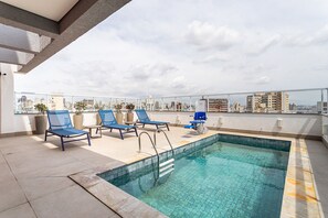 Ein Poolbereich auf dem Dach mit Liegestühlen und freiem Blick auf die Stadtlandschaft.