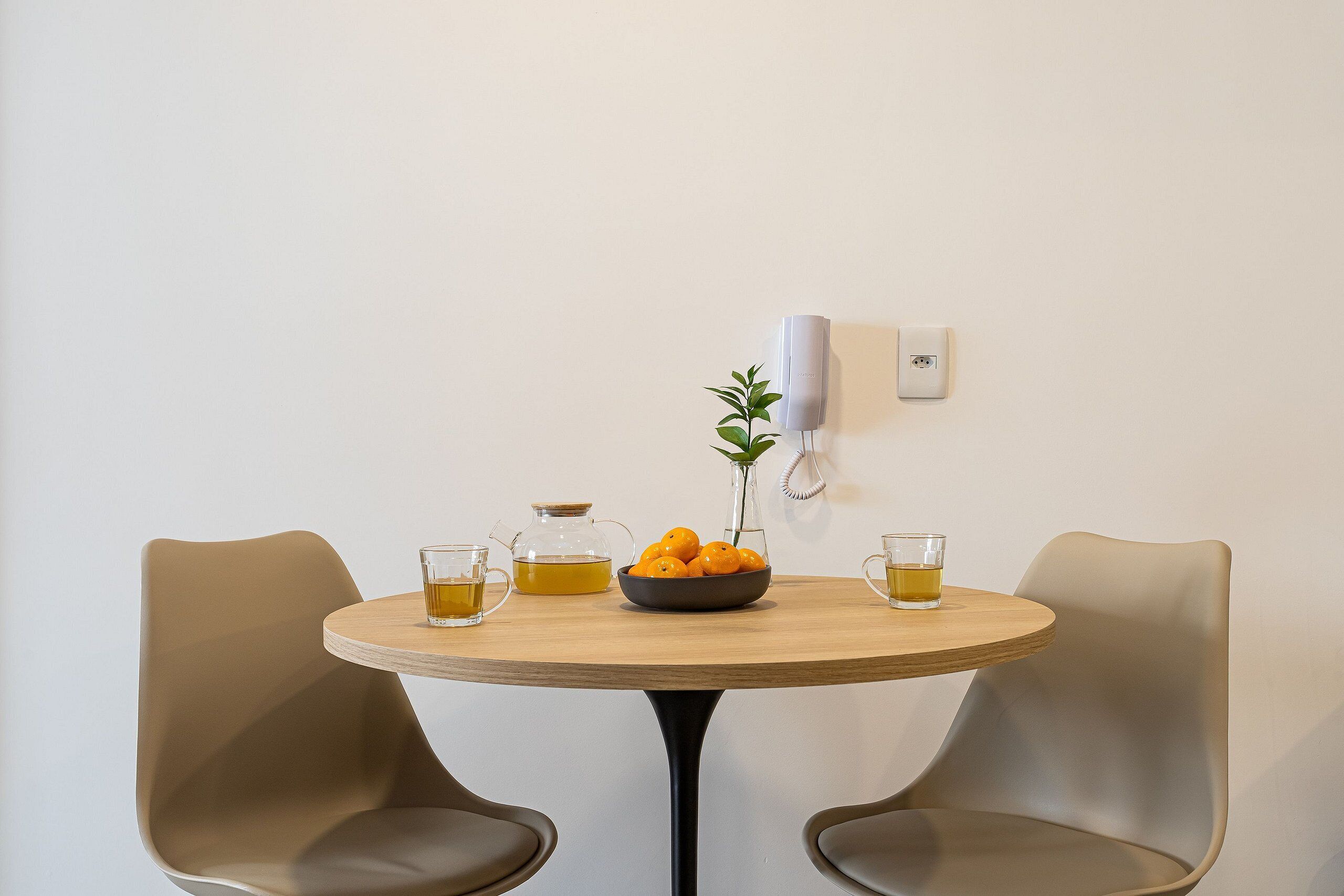 Ein runder Holztisch mit einer Orangenschale und zwei Teetassen, begleitet von zwei modernen Stühlen.