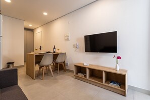 Un soggiorno moderno con una TV a schermo piatto, un tavolino in legno, un divano e un'area pranzo con sedie e un piccolo tavolo.