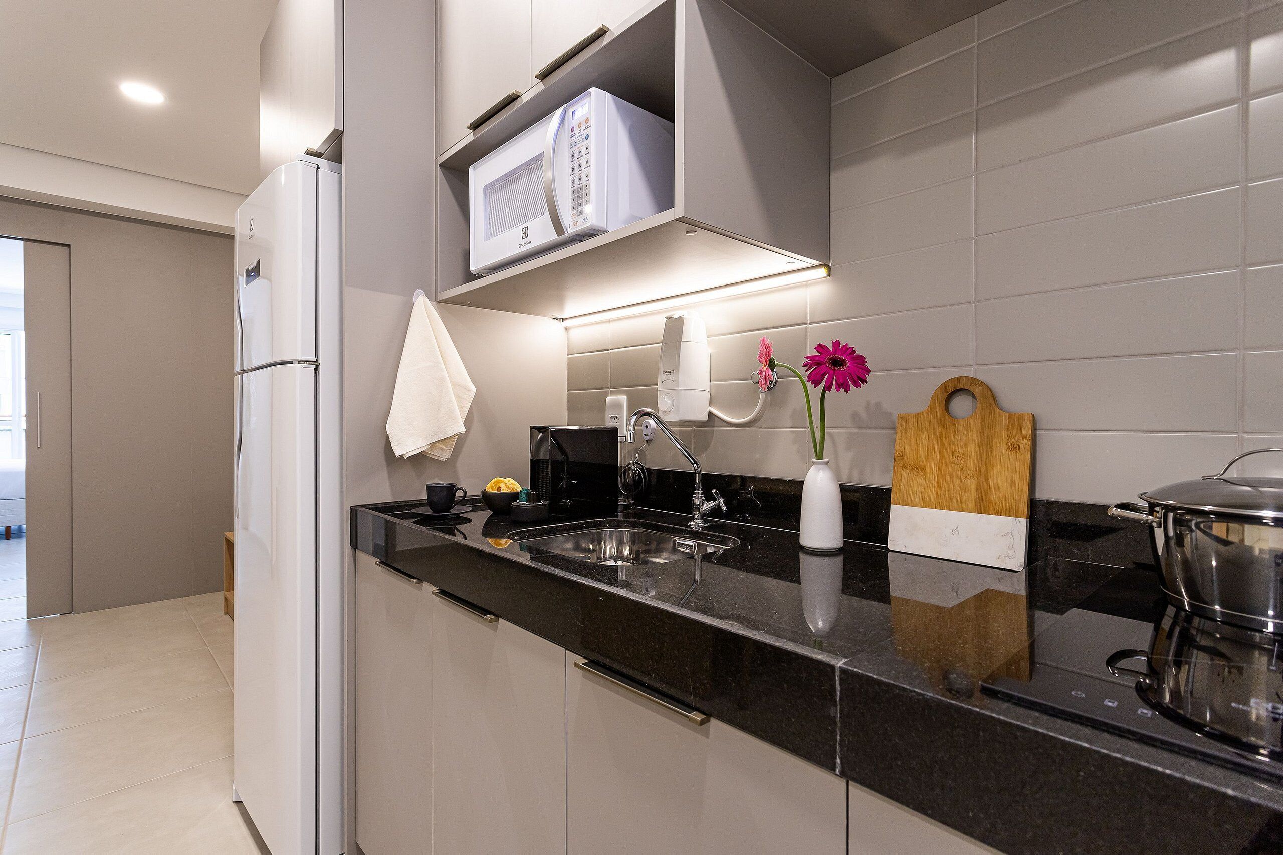 Una cocina moderna con encimera negra, pileta de acero inoxidable y microondas sobre la encimera.