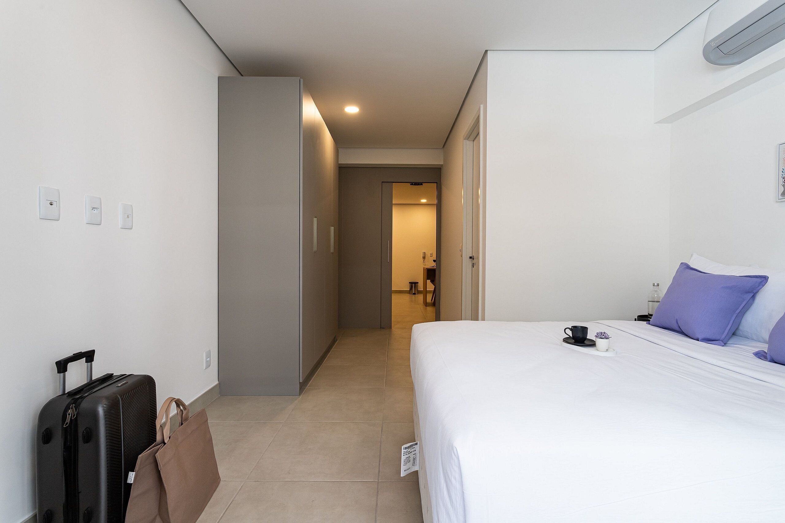 Una habitación de hotel con una cama, una maleta, un bolso y un baño a la vista.