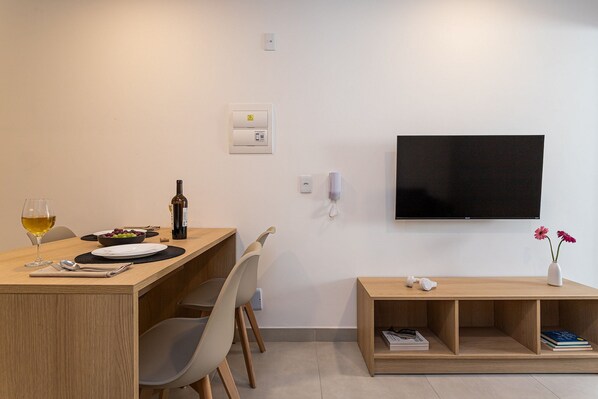 Een moderne woonruimte met een houten eettafel, een flatscreen-televisie aan de muur en een klein boekenrek.
