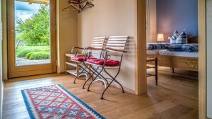 A room with a wooden floor, a patterned rug, a bed with a blue and white checkered bedspread, and a bench with red cushions. - Beautiful vacation apartment on the edge of the Palatinate Mountains (Edenkoben)