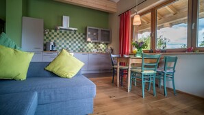A modern living room with a blue sofa, green cushions, a wooden dining table with teal chairs, and a kitchen in the background. - Beautiful vacation apartment on the edge of the Palatinate Mountains (Edenkoben)