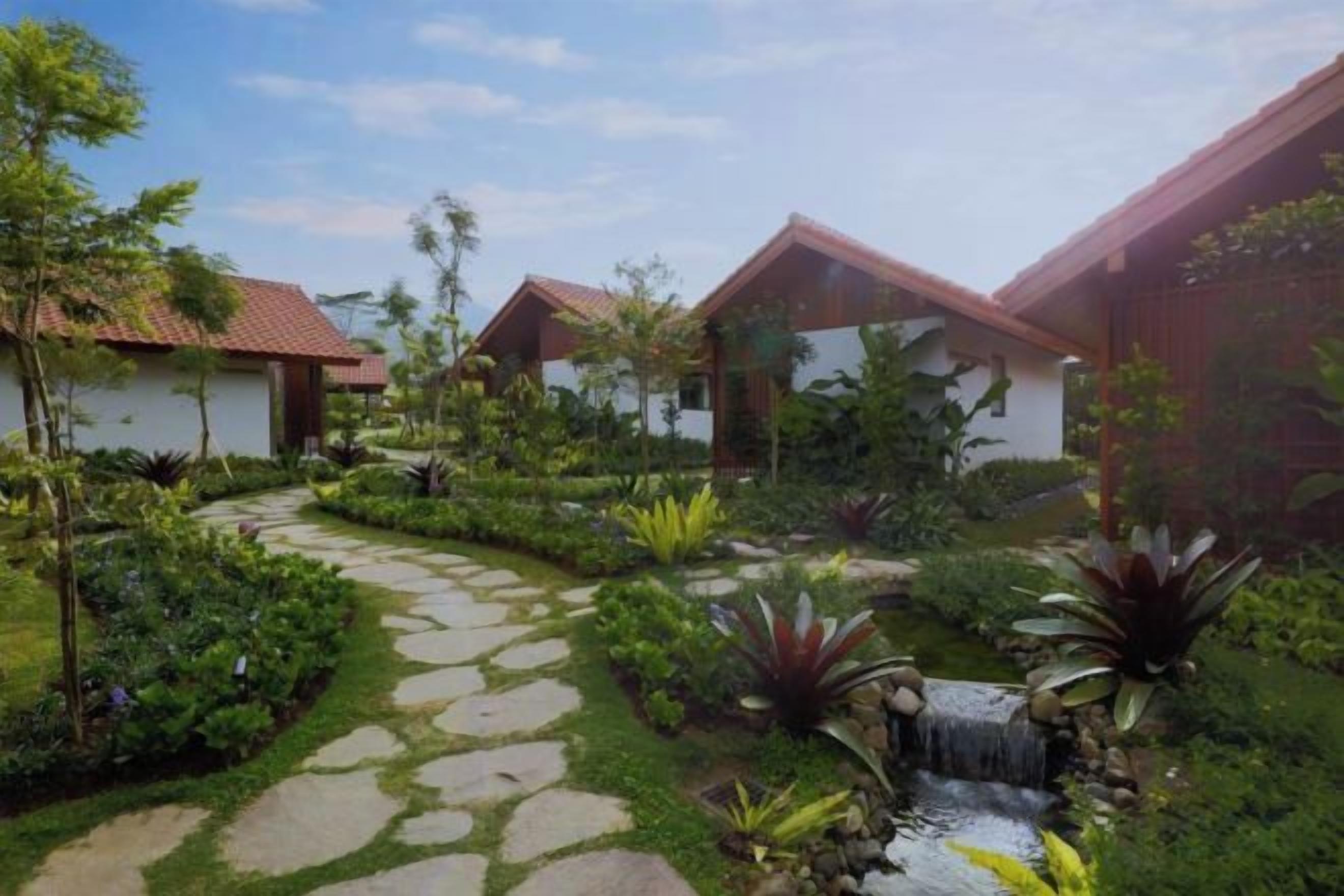 A garden with a stone pathway, a small waterfall, and two buildings with red roofs.