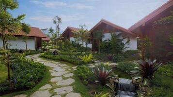A garden with a stone pathway, a small waterfall, and two buildings with red roofs.