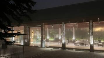 An outdoor seating area with tables and chairs, a water feature, and a building entrance with glass doors.