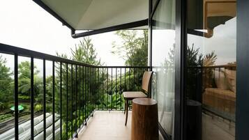 A balcony with a glass partition, a wooden chair, a small round table, and a view of greenery.