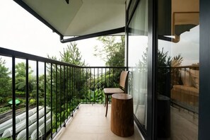 Un balcón con una barandilla de vidrio, una silla de madera, una mesita redonda y vista a zonas verdes.