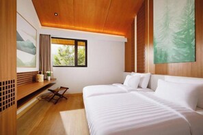 Habitación de hotel moderna con techo de madera, cama grande, escritorio con silla y ventana con vista a árboles.