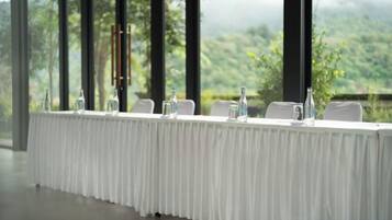 A long table with chairs, water bottles, and a glass pitcher, set against a backdrop of a mountainous landscape through large windows.
