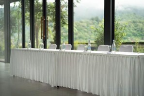 A long table with chairs, water bottles, and a glass pitcher, set against a backdrop of a mountainous landscape through large windows. - Dusun Bedugul Asri (Bali)