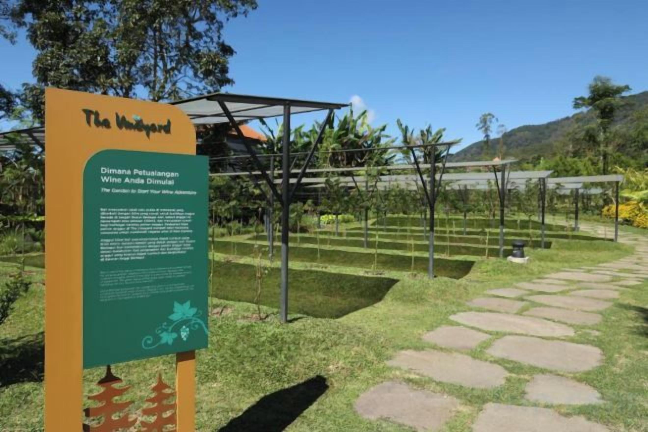 Un cartel con texto y un jardín con senderos y plantas.