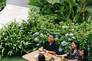 A dining table with plates, cups, and a bottle in a lush garden setting.