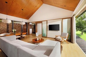 A modern living room with a large sofa, a dining area with wooden furniture, and a TV mounted on the wall. - Dusun Bedugul Asri (Bali)