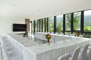 Un salón de conferencias con una larga mesa, sillas, una televisión y ventanas amplias con vistas.