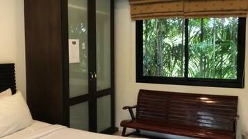 Ein Zimmer mit einem Bett, einer hölzernen Bank, einem Fenster mit Blick auf Grünflächen und einer Milchglasschiebetür.