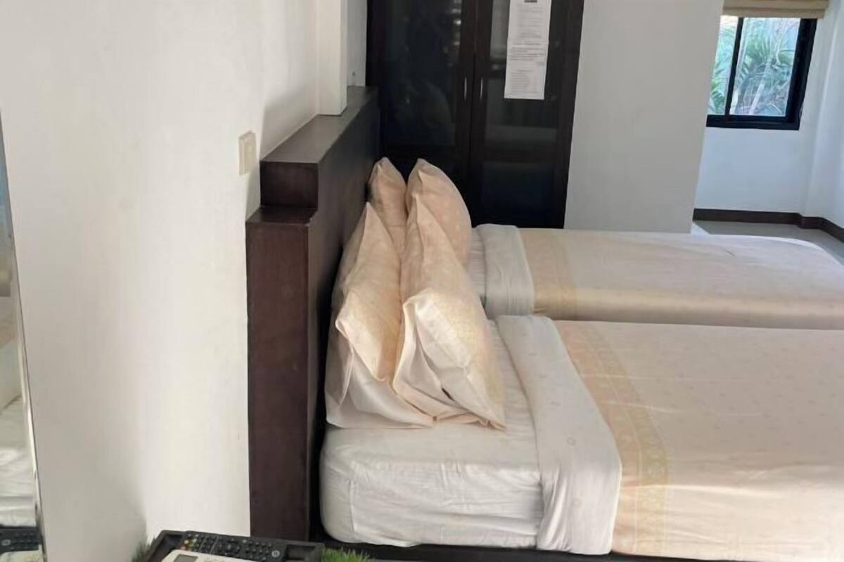 Egy szállodai szoba két ágyjal, fafejtámlával, kilátással rendelkező ablakkal és egy kis növényt tartalmazó éjjeliszekrényjel.