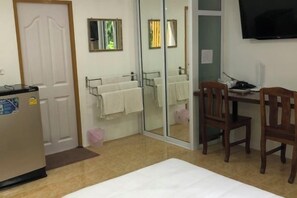 A hotel room with a bed, a desk with a chair, a TV, a mirror, and a door. - Pichawaree Resort (Si Thep)