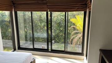 Ein Schlafzimmer mit großem Fenster, einem Bett und Blick ins Grüne.