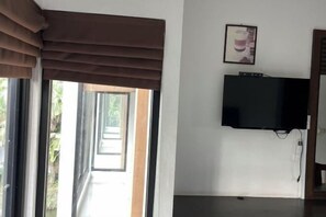 A room with a television mounted on the wall, a window with brown curtains, and a door leading outside. - Pichawaree Resort (Si Thep)