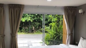 A hotel room with a bed, curtains, and a view of greenery outside. - Pichawaree Resort (Si Thep)
