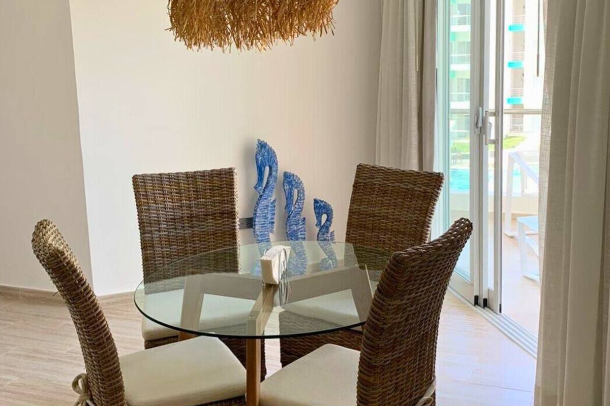 A dining area with a glass table surrounded by wicker chairs with white cushions.