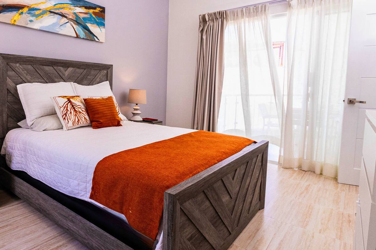 A neatly made bed with a wooden headboard, two bedside lamps, and a colorful abstract painting on the wall.