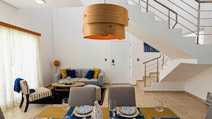 A modern living room with a dining area, a staircase, and a large wooden pendant light. - Maple Beach Residences Punta Cana  (Punta Cana)