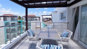 A covered outdoor seating area with a table and chairs, overlooking a residential area with multiple buildings. - Maple Beach Residences Punta Cana  (Punta Cana)