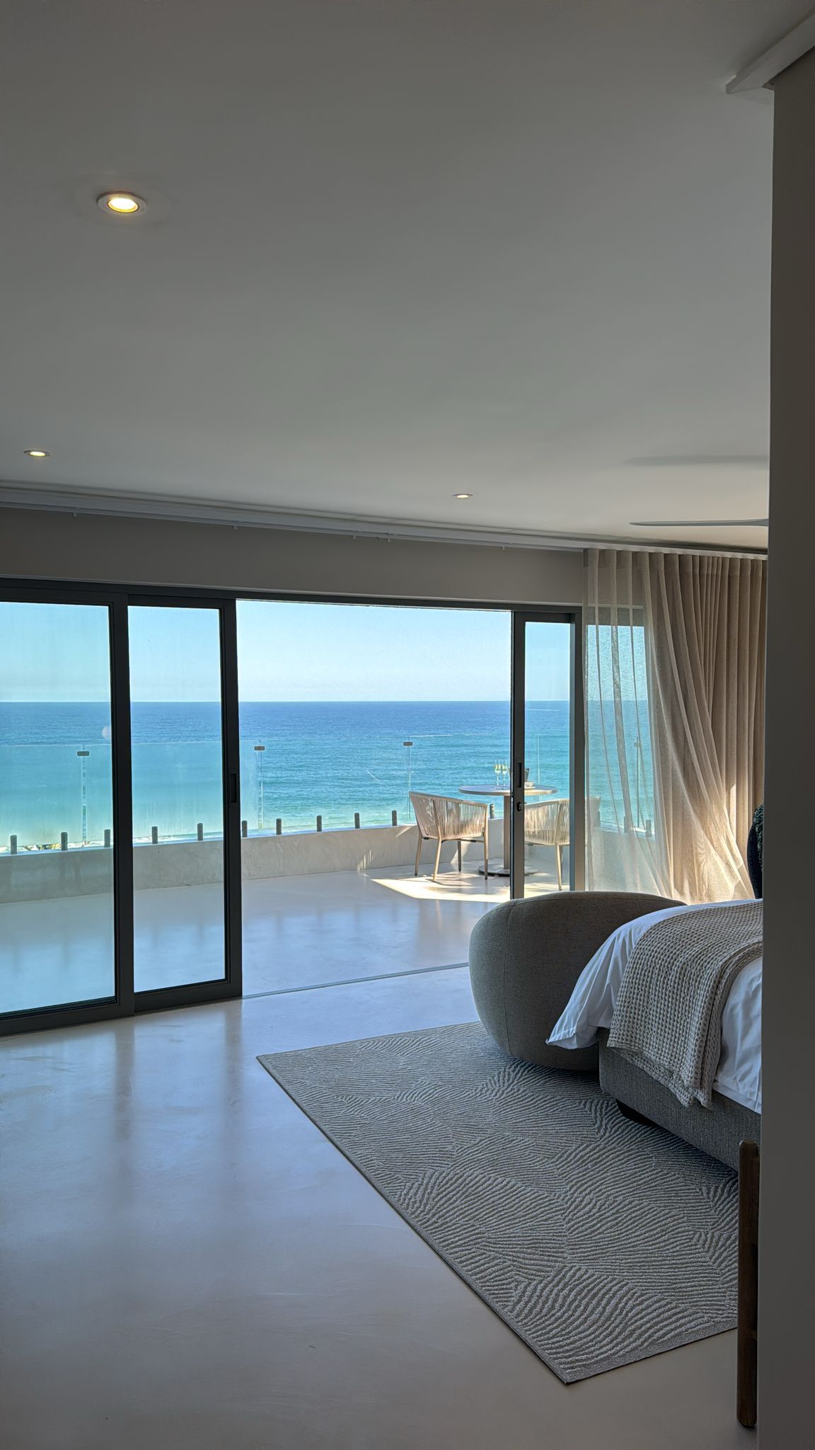 Quarto com grande janela vista para o mar, cama e área de estar com mesa.