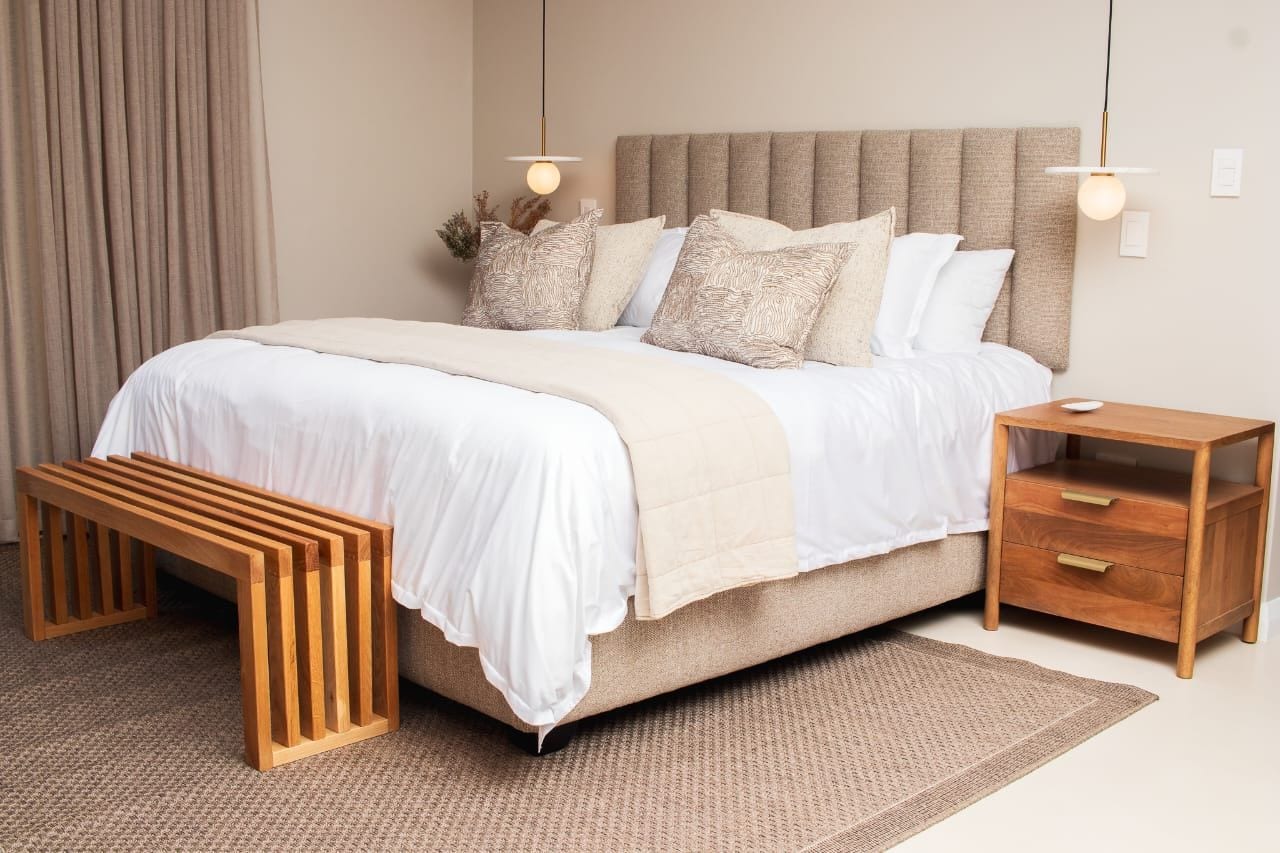 Un dormitorio con cama, mesitas de noche, un banco y una lámpara colgante.