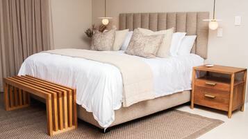 Un dormitorio con cama, mesitas de noche, un banco y una lámpara colgante.