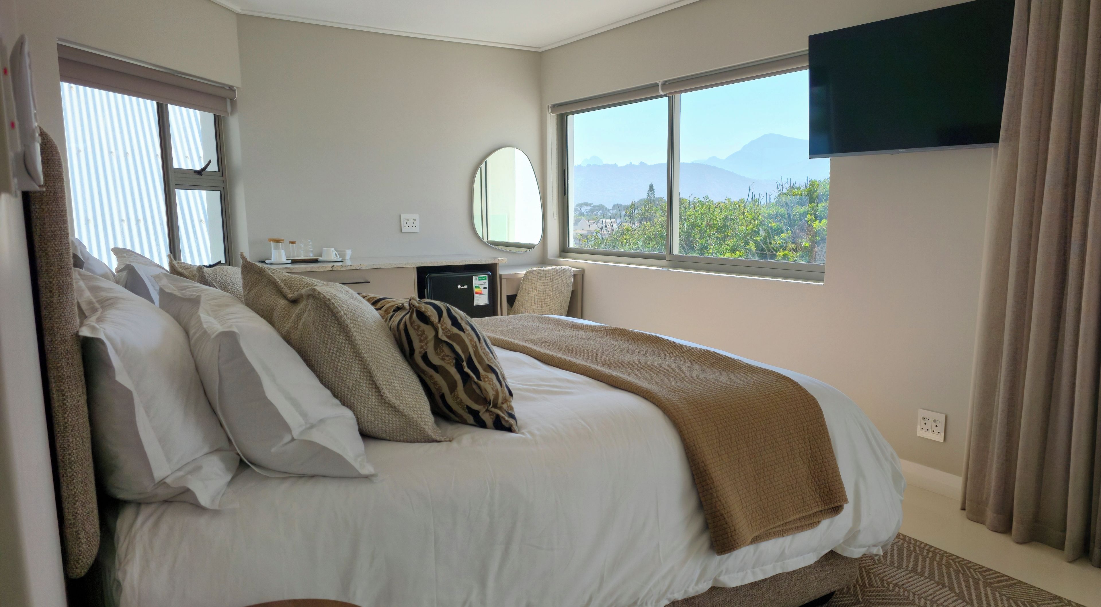 Habitación de hotel con cama, escritorio, silla, televisión y ventana con vistas a montañas.