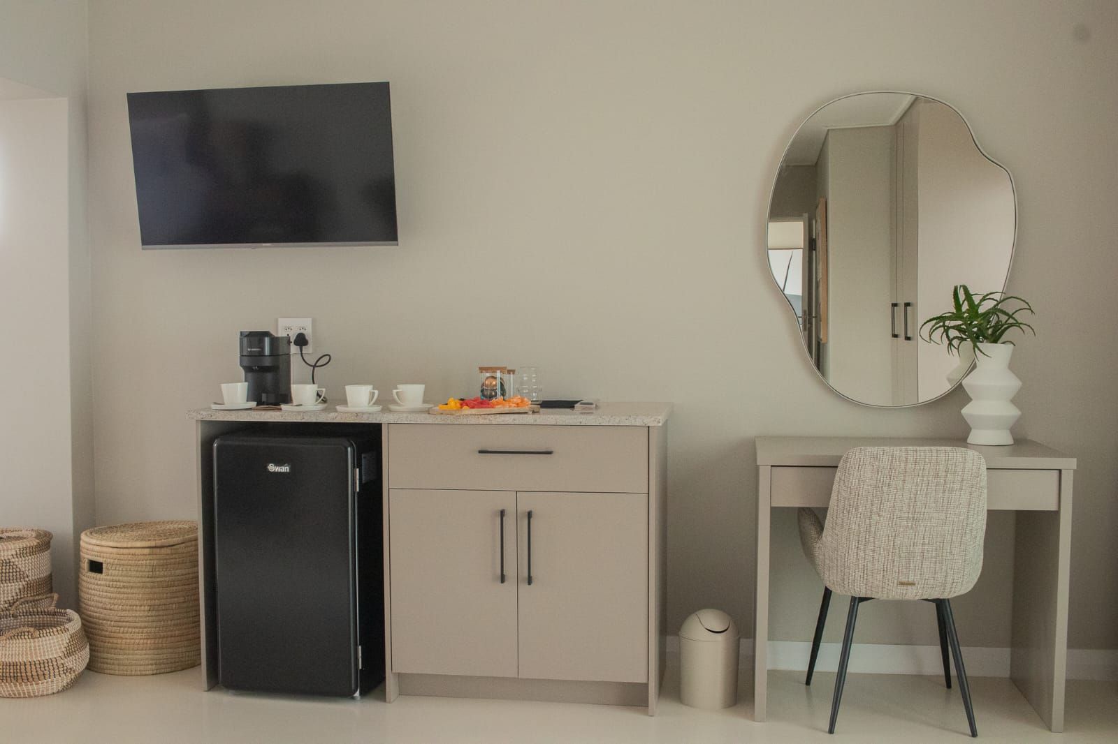 Una kitchenette con un refrigerador negro, una cafetera y una pequeña encimera con tazas y un plato de fruta.