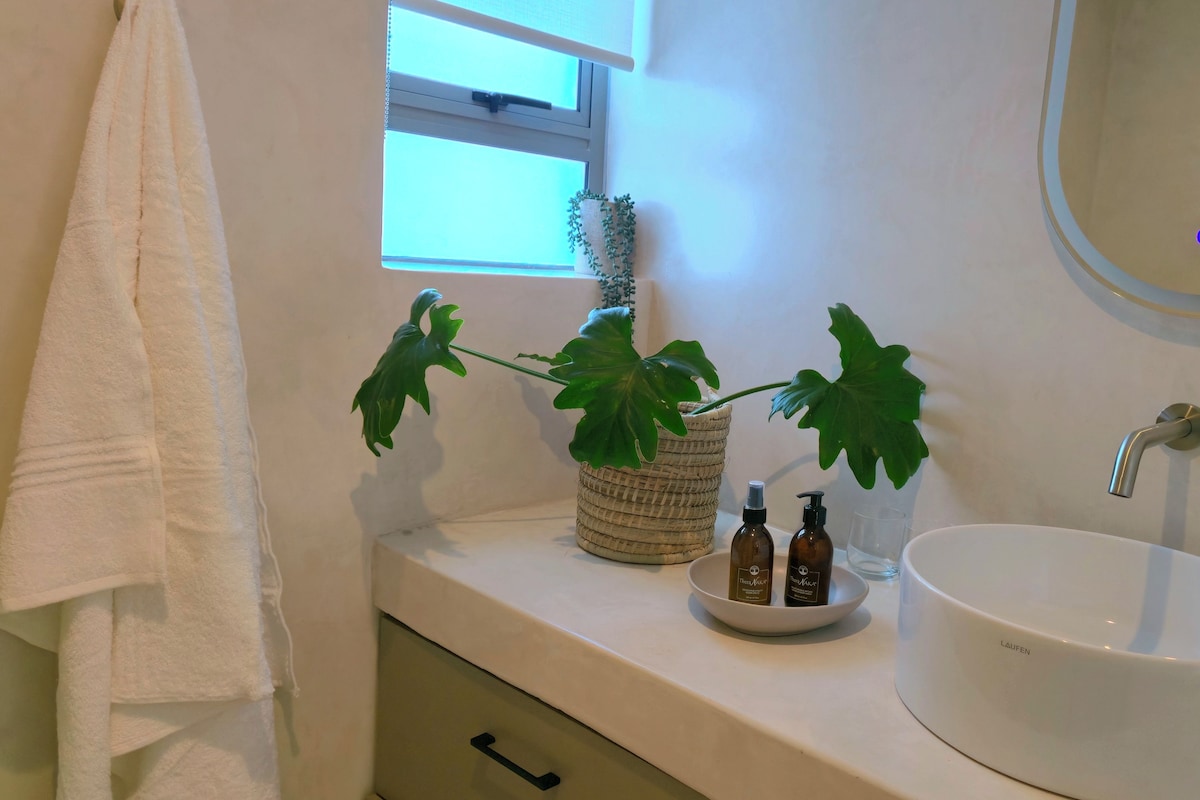 A bathroom with a white sink, a mirror, a window, and a potted plant.