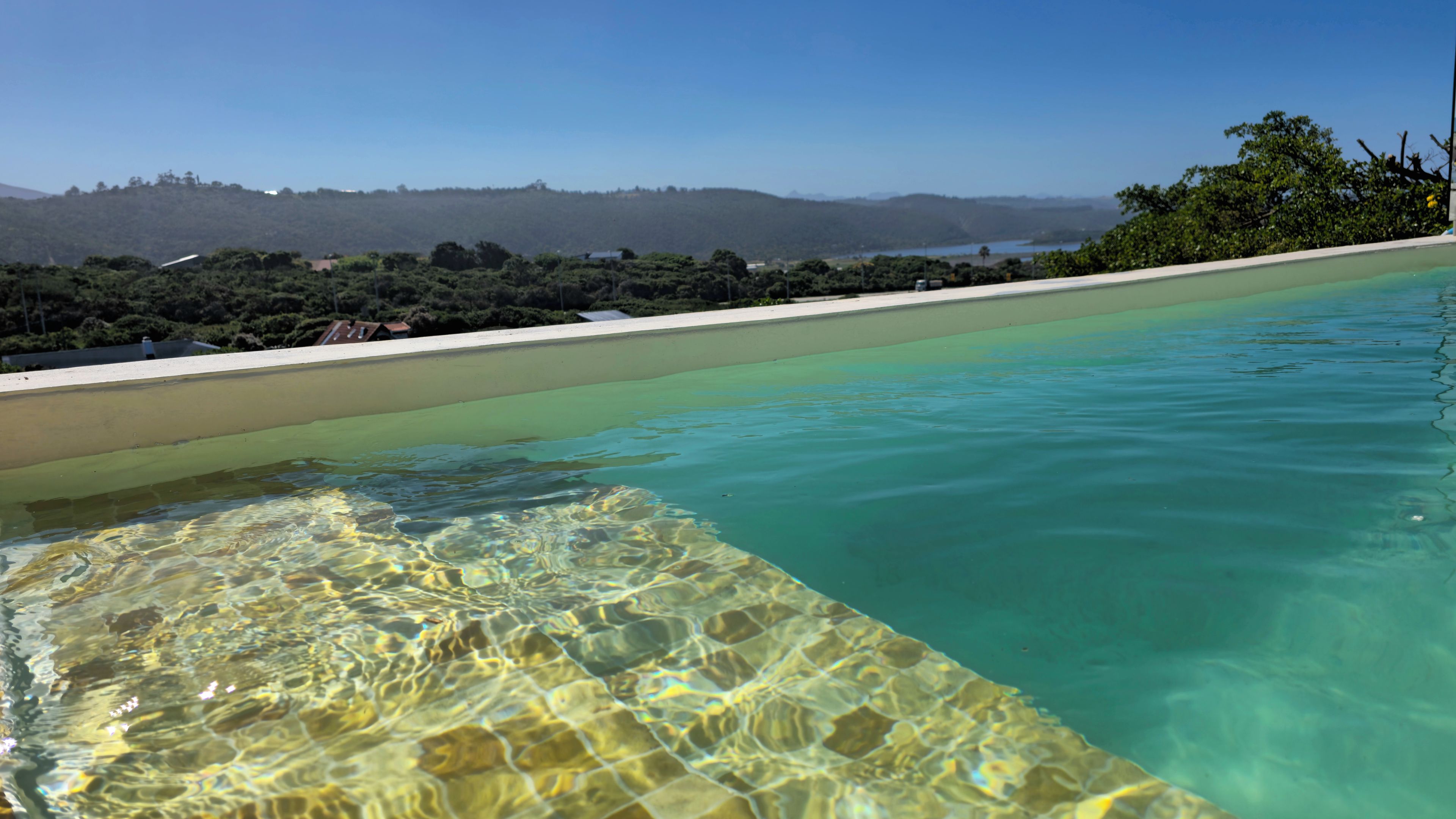 Una piscina cristalina con vista a una playa y colinas al fondo.