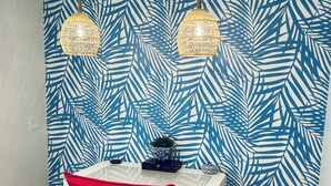 Une pièce avec une table blanche, une chaise rouge et un mur orné d’un motif de feuilles bleues. Deux lampes sont suspendues au-dessus de la table.