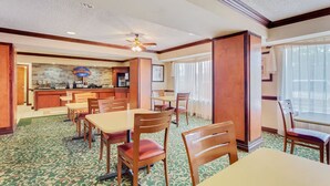 A hotel dining area with a breakfast bar, multiple tables and chairs, and a patterned carpet. - Staywell Inn (Kalamazoo)