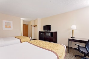 A hotel room with two beds, a desk with a lamp, a television, and a microwave.